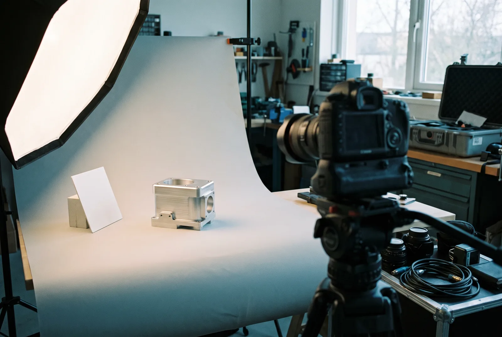 A precision-machined component lit on a seamless backdrop in a photography studio, camera on a tripod alongside